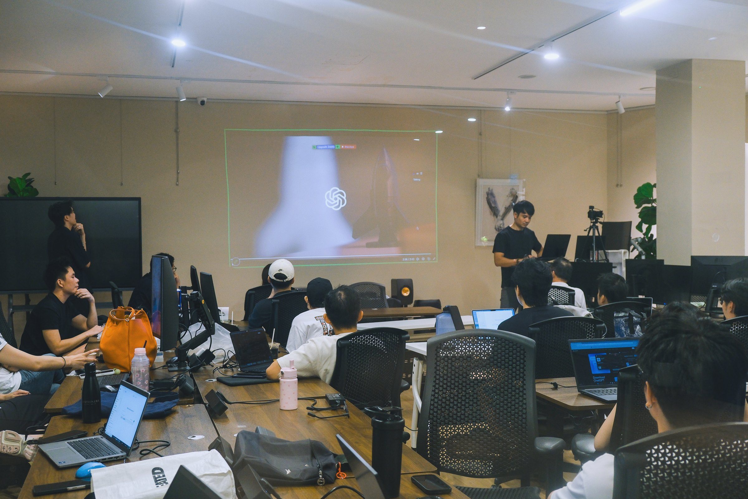 The room at work: learners at their laptops while the instructor stands by the projected screen