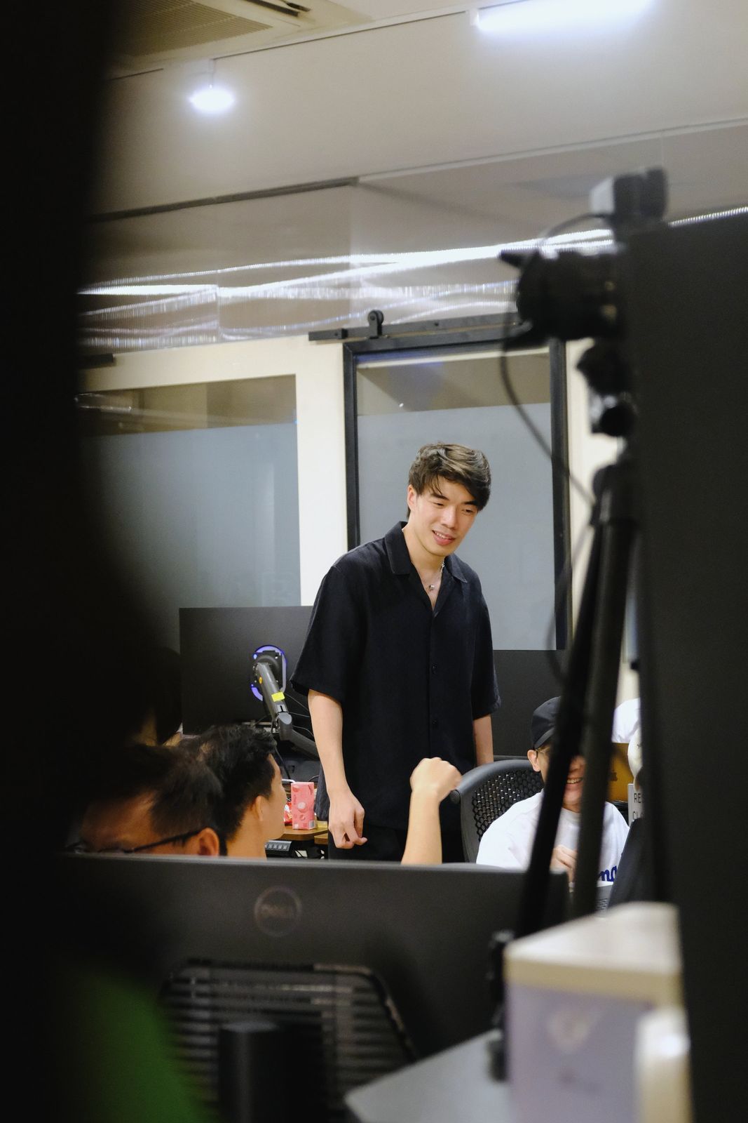 An instructor talks with learners at their desks, seen past a camera on a tripod