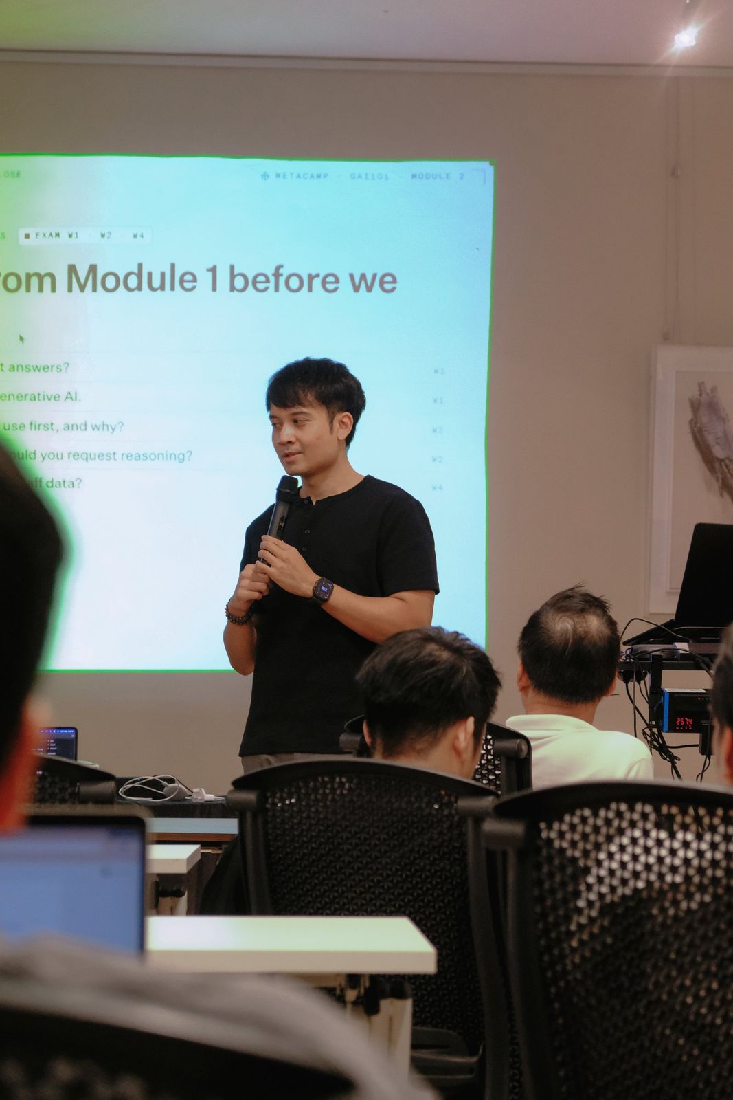 An instructor speaks to the class with a microphone in front of a projected slide