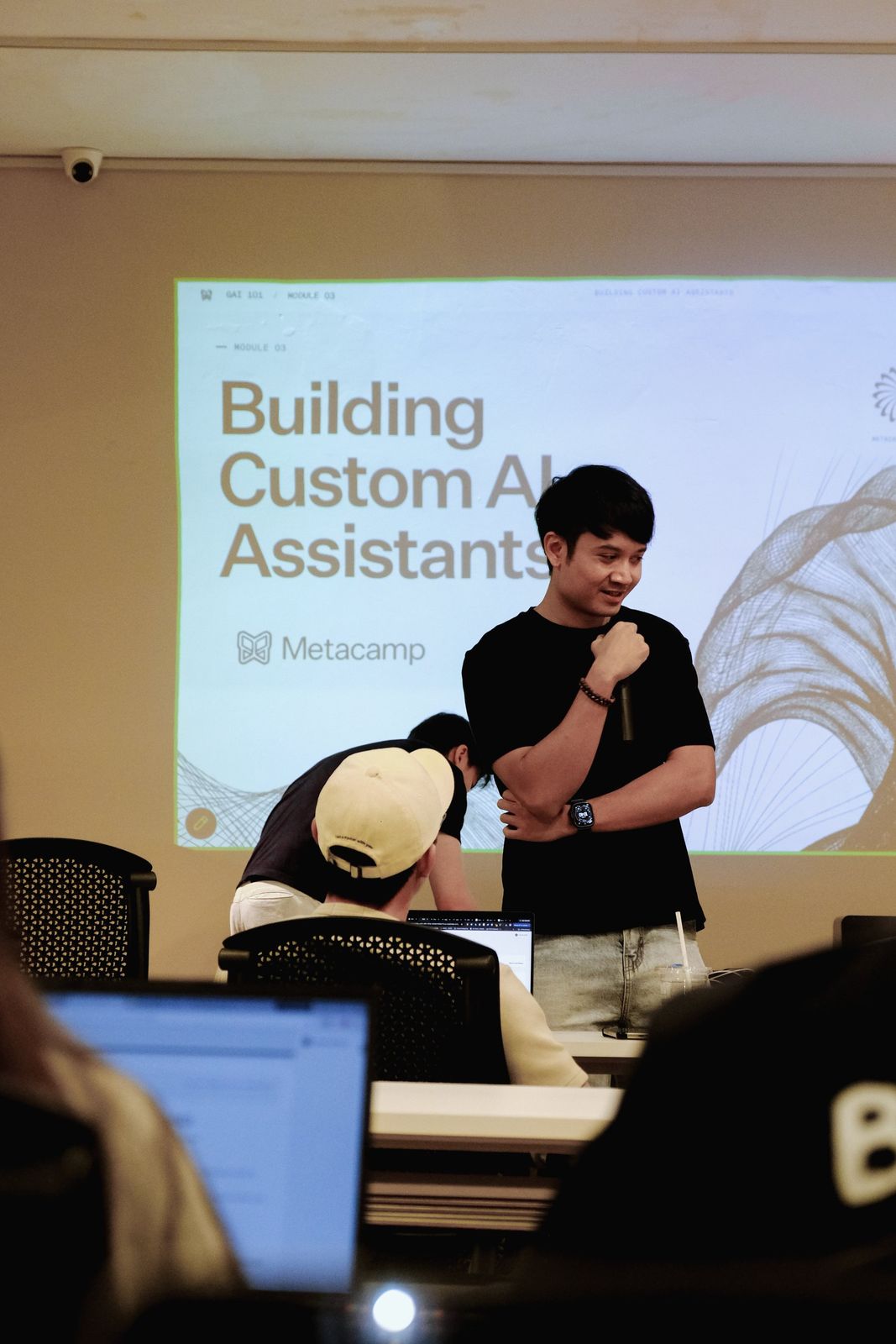 An instructor presents a slide on building custom AI assistants while a learner works at a laptop